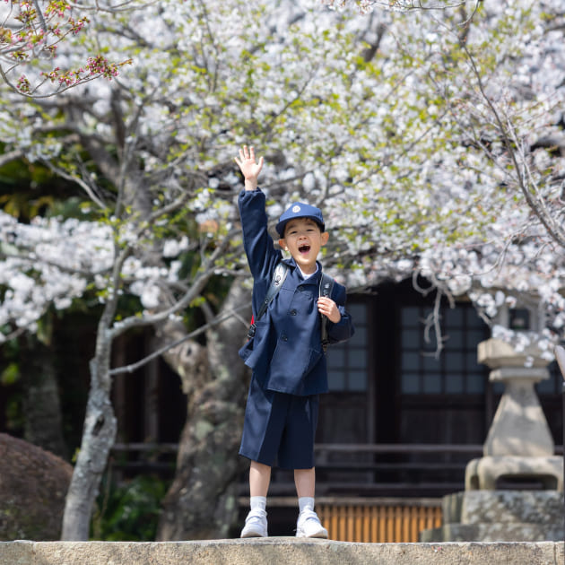 卒業入学撮影　ランドセルを背負って右手を挙げている男の子