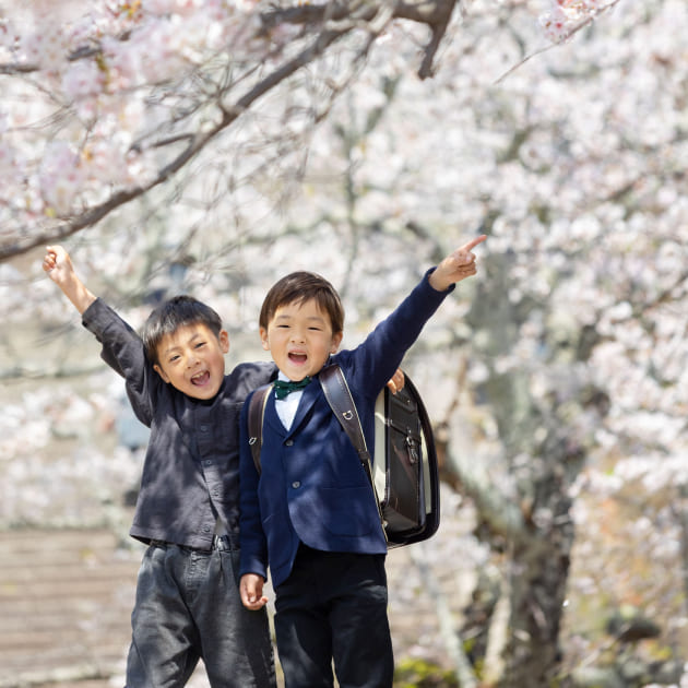 桜の下で手を挙げる子ども2人の春の記念写真